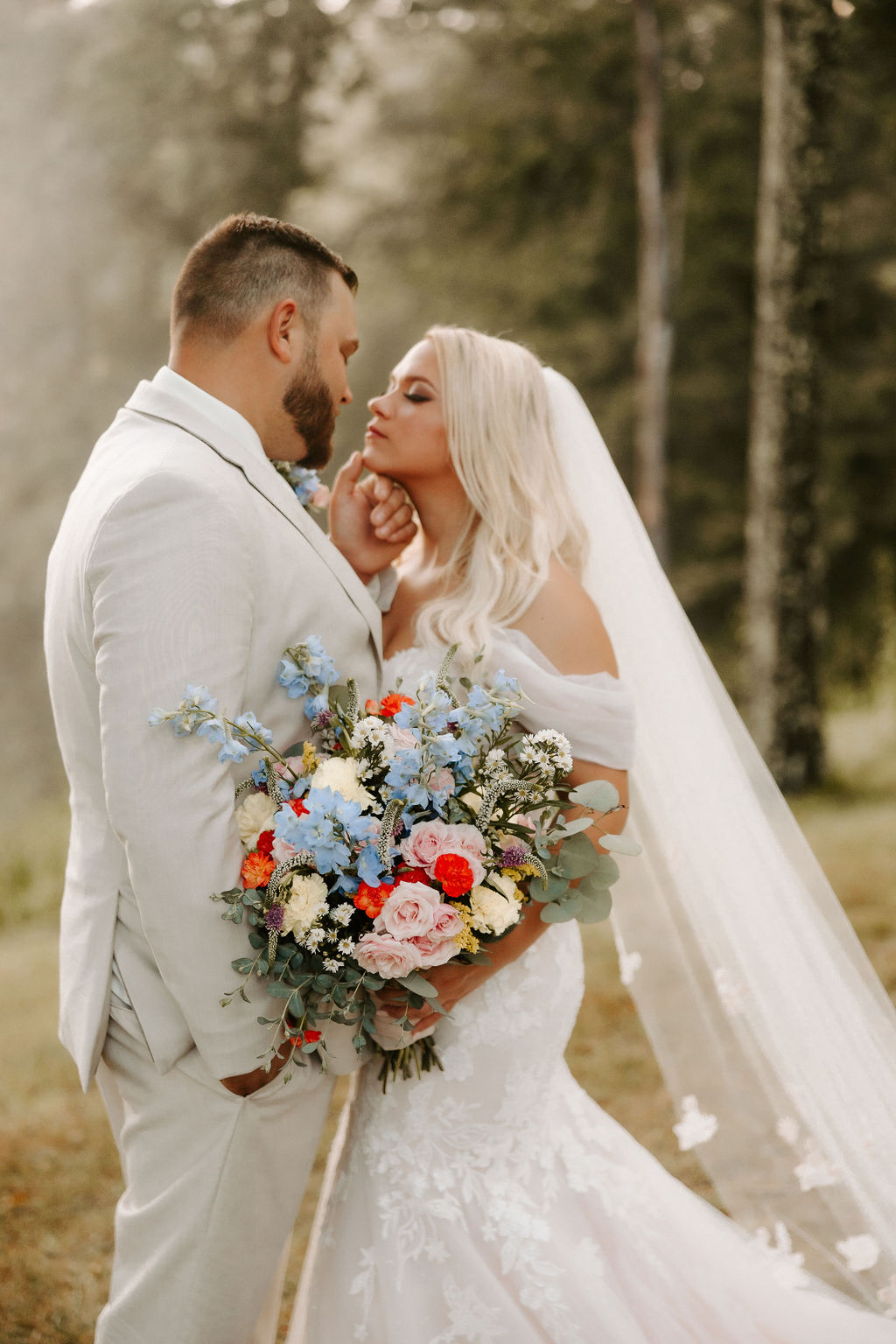 Groom caresses bride's chin with trees in background